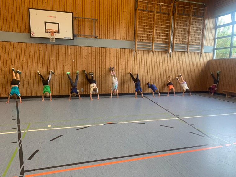 Eine Reihe Kinder macht Handstand an der Hallenwand