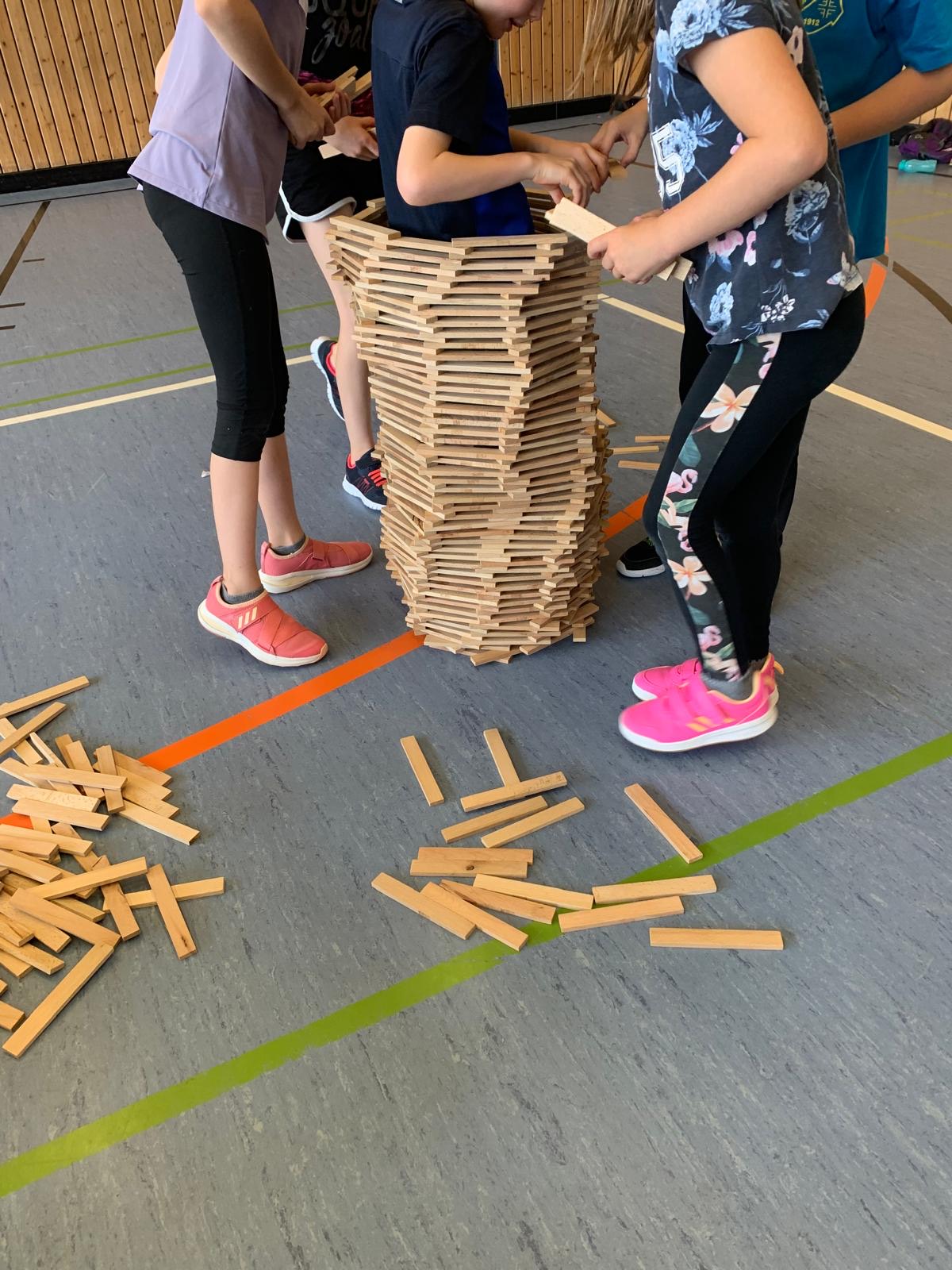 Kinder bauen in der Halle gemeinsam einen hohen Turm aus Holzbausteinen