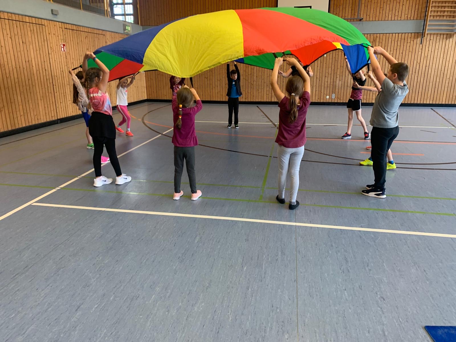 Kinder heben in der Turnhalle gemeinsam ein buntes Schwungtuch