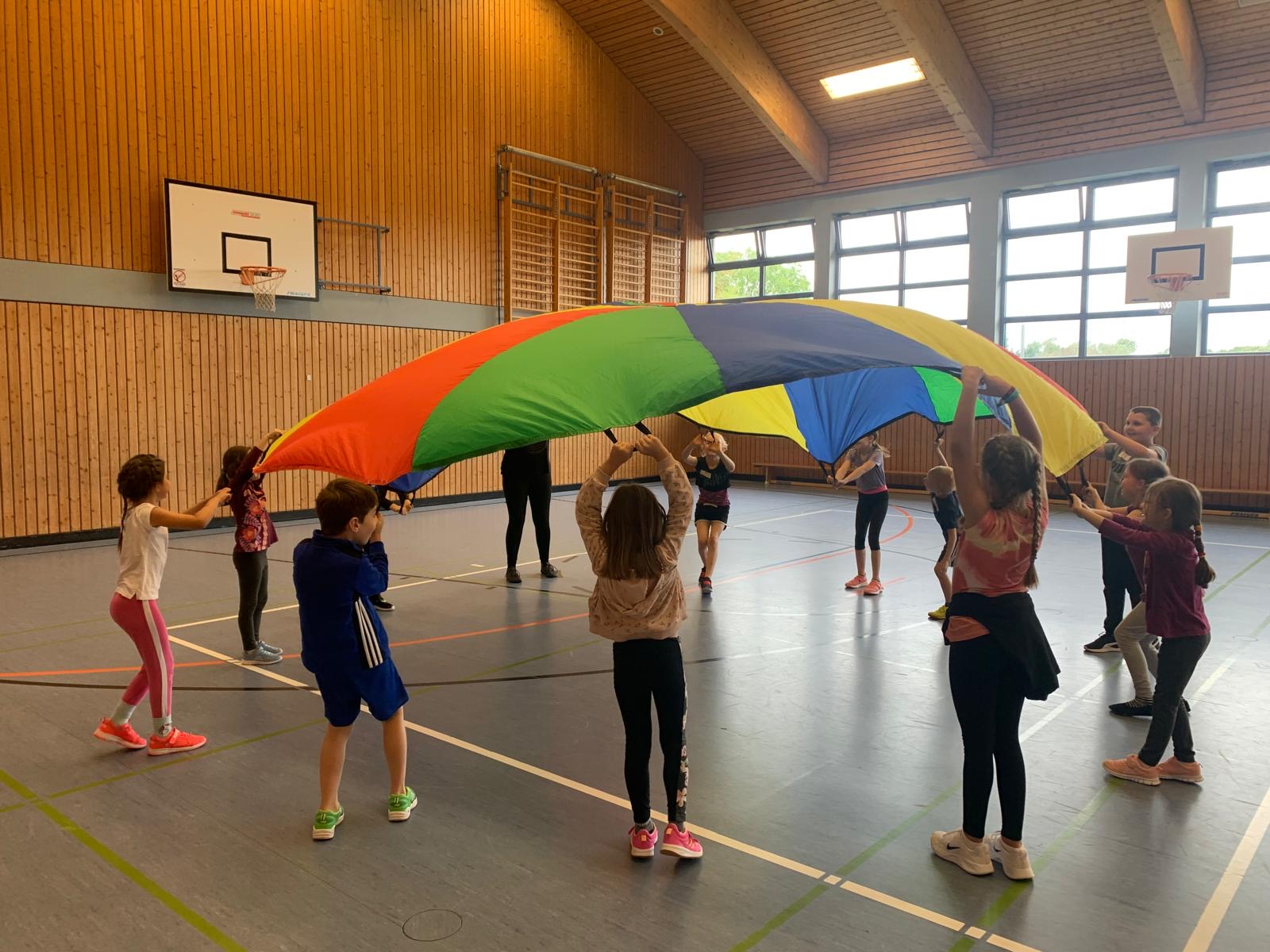 Kinder stehen im Kreis und lassen ein Schwungtuch über sich steigen