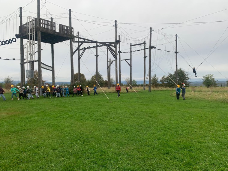 Eine Kindergruppe mit Helmen zieht gemeinsam am Seil vor dem Hochseilgarten