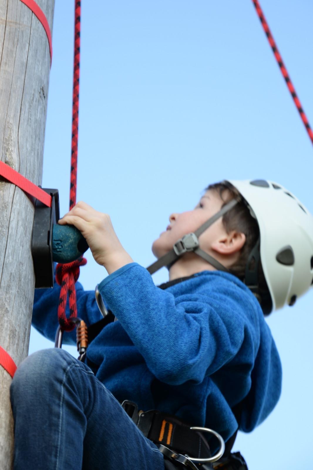 Junge mit Helm greift beim Stammklettern nach dem nächsten Griff